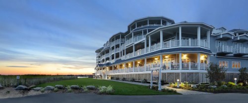 A coastal hotel at sunset, featuring multiple balconies and a landscaped lawn in the foreground.