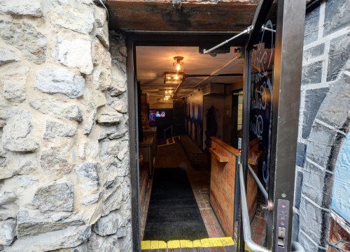A view of a stone entrance leading into a dimly lit hallway with wooden accents and a glimpse of a TV in the background.