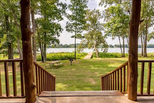 View from a porch overlooking a serene lake, surrounded by trees and a grassy area with a picnic table.
