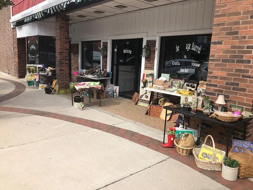 A storefront with tables displaying various vintage and craft items, surrounded by brick walls and a sidewalk.