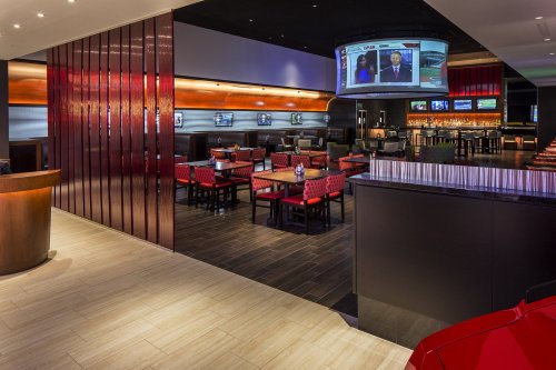 Modern restaurant interior with red and black decor, tables, and a large screen displaying news.