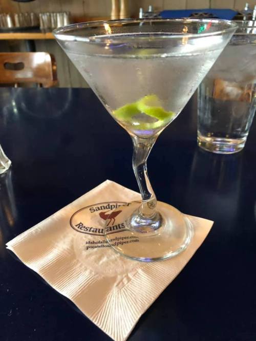 A martini with a lime twist sits on a napkin at a restaurant, with a glass of water in the background.