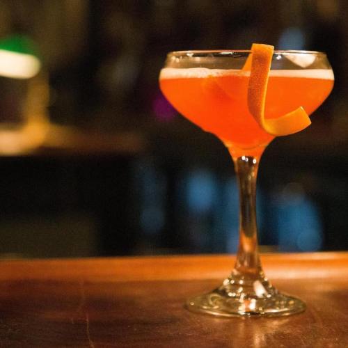 A vibrant orange cocktail garnished with a twist of orange peel, served in a stylish glass on a wooden bar.