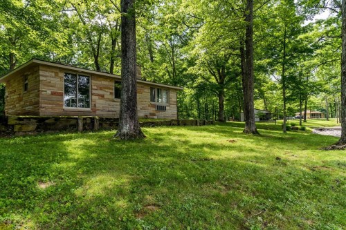 A single-story house surrounded by lush green trees and grass, set in a peaceful, wooded area.
