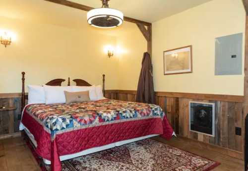 Cozy bedroom with a quilted bedspread, wooden accents, and warm lighting. A fireplace adds charm to the space.