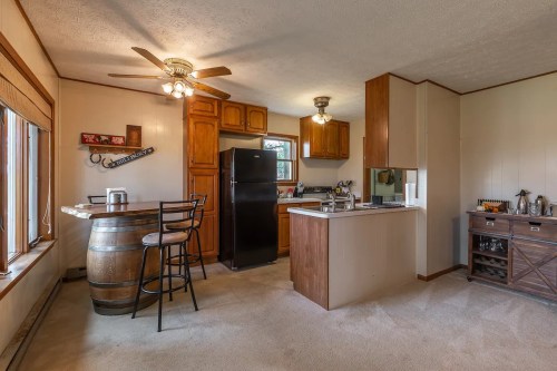 Cozy kitchen with wooden cabinets, a black fridge, a bar with stools, and a small dining area. Bright and inviting space.