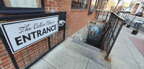 A brick building with a sign reading "The Collar Door Entrance" above a staircase leading down to a lower level.