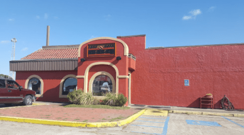 A red restaurant building with a sign, featuring arched windows and a parking lot under a clear blue sky.