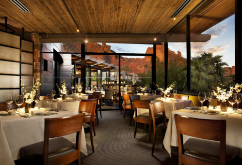 Elegant restaurant interior with wooden accents, tables set for dining, and a scenic view of mountains at sunset.