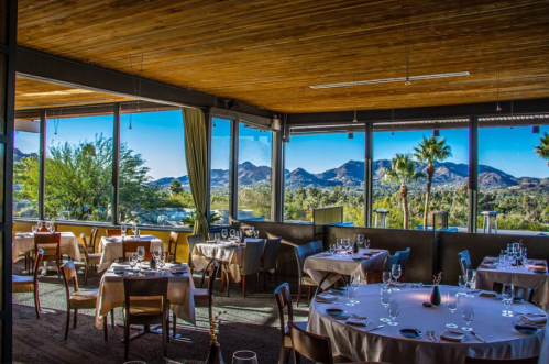Elegant restaurant interior with tables set for dining, featuring large windows showcasing a scenic mountain view.