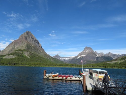 A scenic view of a lake with a dock, boats, and mountains under a clear blue sky.