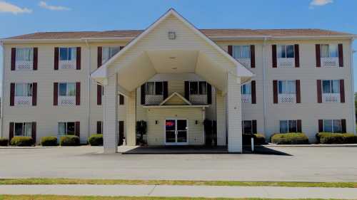 A two-story hotel with a covered entrance, large windows, and landscaped shrubs under a clear blue sky.