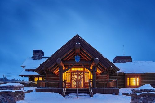 A cozy log cabin with warm lights glowing, surrounded by snow under a twilight sky.