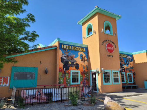 Colorful exterior of a Mexican restaurant with murals, a tower, and a sign indicating it's open. Clear blue sky above.