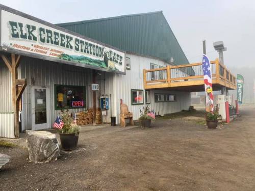 Exterior of Elk Creek Station Cafe, featuring a sign, flags, and a wooden deck, set in a foggy environment.