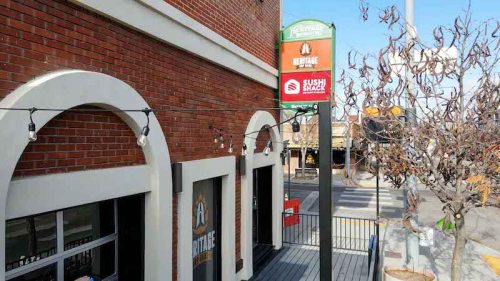Exterior view of a brick building with a sign for "Heritage" and "Sushi Shack," featuring string lights and a tree.