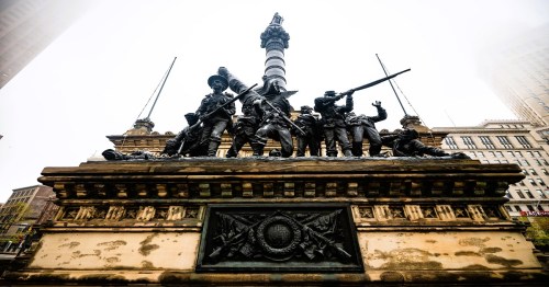A detailed bronze monument featuring soldiers in various poses, set against a foggy city backdrop.