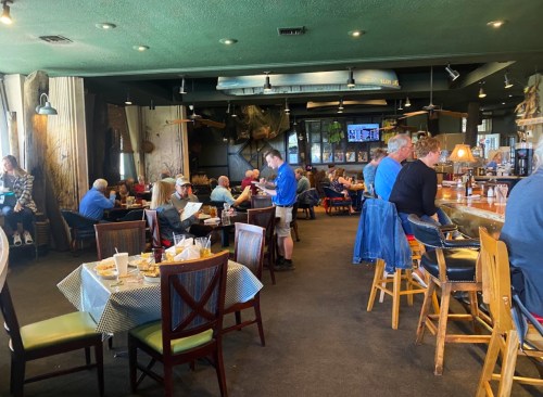 A busy restaurant interior with diners at tables and a bar, featuring a casual atmosphere and green ceiling.