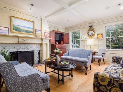 Cozy living room with blue patterned furniture, a fireplace, and large windows, featuring a coffee table and decorative artwork.