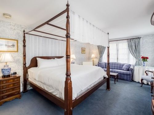 A cozy bedroom featuring a four-poster bed, blue carpet, and a sitting area with a couch and decorative lamps.