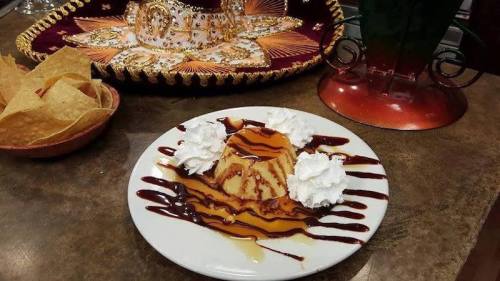A dessert plate with flan drizzled in chocolate and caramel sauce, topped with whipped cream, alongside tortilla chips.