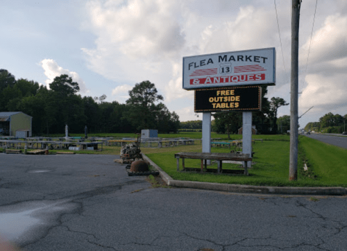 Sign for a flea market with "Free Outside Tables" displayed, surrounded by grassy areas and trees in the background.