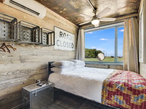 Cozy bedroom with a bed, vintage decor, and a large window overlooking greenery.