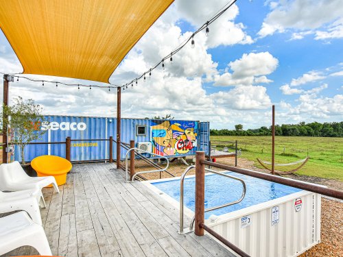 A sunny outdoor space featuring a small pool, colorful shipping container, and lounge chairs under a shaded canopy.