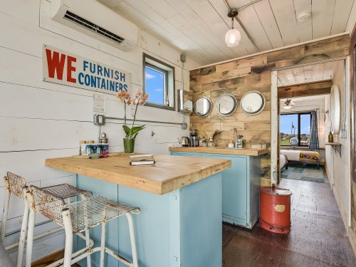 Cozy interior of a container home featuring a wooden kitchen island, mirrors, and rustic decor.