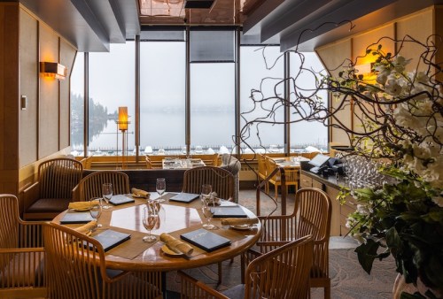 Elegant dining room with a round table set for a meal, large windows showcasing a foggy lake view.