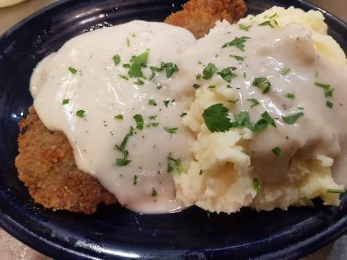 A plate of fried chicken covered in creamy gravy, served with a side of mashed potatoes and garnished with parsley.
