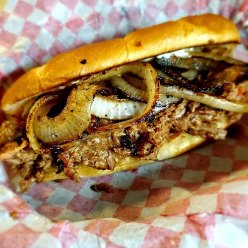 A close-up of a sandwich filled with grilled meat and onions, served in a checkered paper wrapper.