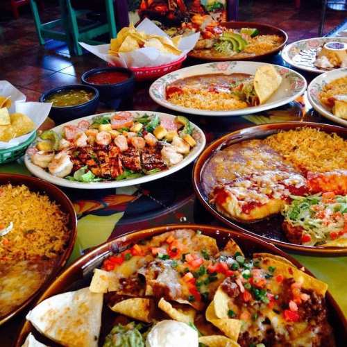 A vibrant spread of Mexican dishes, including tacos, enchiladas, rice, and guacamole, served in a colorful restaurant setting.