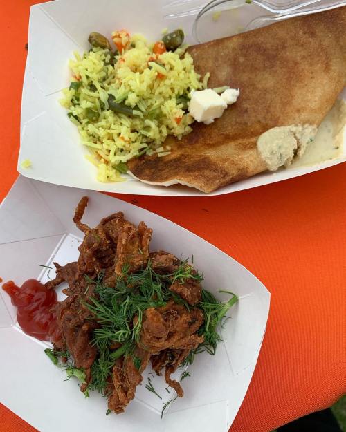 A plate of colorful rice with vegetables, a dosa, and a serving of crispy fried onions topped with herbs and ketchup.