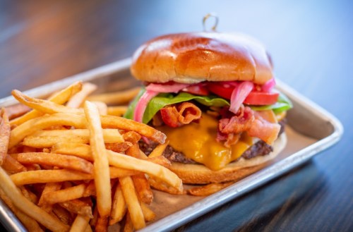 A juicy cheeseburger topped with bacon, lettuce, tomato, and pickled onions, served with a side of crispy fries.