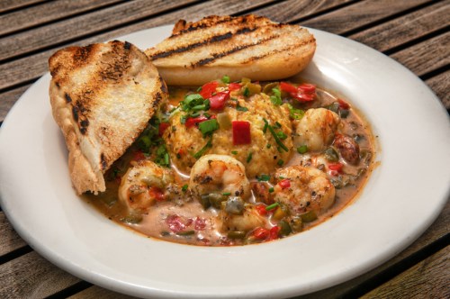 A plate of shrimp and grits topped with herbs, served with two slices of grilled bread on the side.