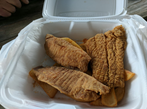 A takeout container with three pieces of fried fish on a bed of golden-brown fries.