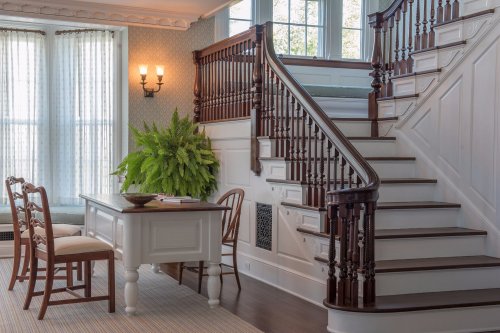 A bright interior featuring a staircase, a wooden table with chairs, and a large potted plant by the window.