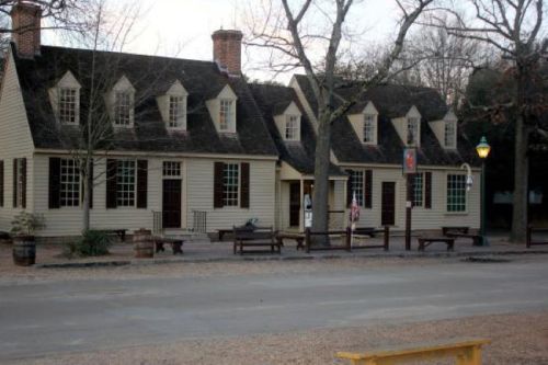 Historic building with a sloped roof, multiple windows, and a porch, surrounded by trees and a gravel path.