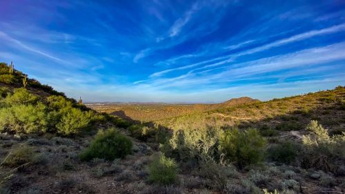 A scenic view of a desert landscape with rolling hills, green vegetation, and a blue sky with wispy clouds.