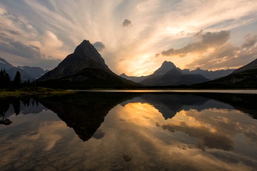 A serene mountain landscape at sunset, with dramatic clouds reflected in a calm lake.
