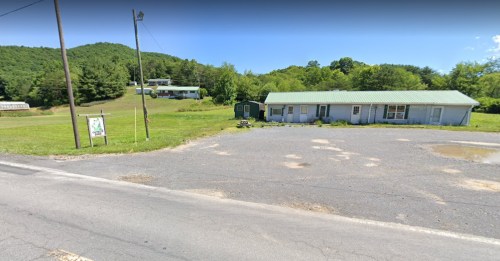 A rural scene featuring a green-roofed building, grassy area, and hills in the background.
