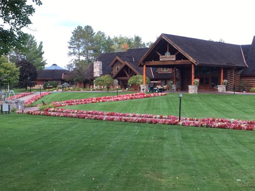 A beautifully landscaped entrance to a lodge, featuring vibrant flower beds and a well-maintained lawn.