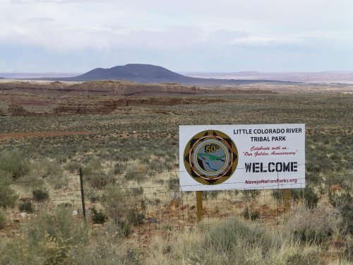 Sign for Little Colorado River Tribal Park with a scenic view of a distant mountain and desert landscape.