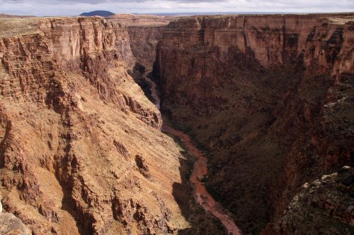 A vast canyon with steep, rocky walls and a winding river at the bottom, surrounded by arid landscape.