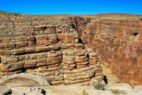A vast canyon landscape with layered rock formations under a clear blue sky.