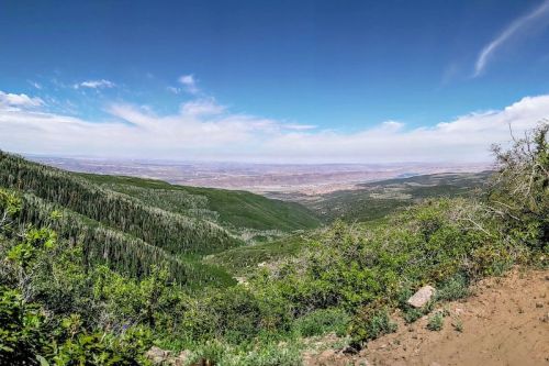 A panoramic view of lush green mountains and valleys under a bright blue sky with scattered clouds.
