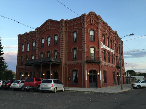 Historic red brick building with ornate architecture, parked cars in front, and a clear sky in the background.