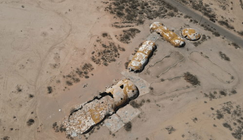 Aerial view of unique, colorful structures in a desert landscape, surrounded by sparse vegetation and winding paths.