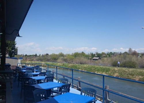 Outdoor dining area with blue tables overlooking a river and green landscape under a clear blue sky.